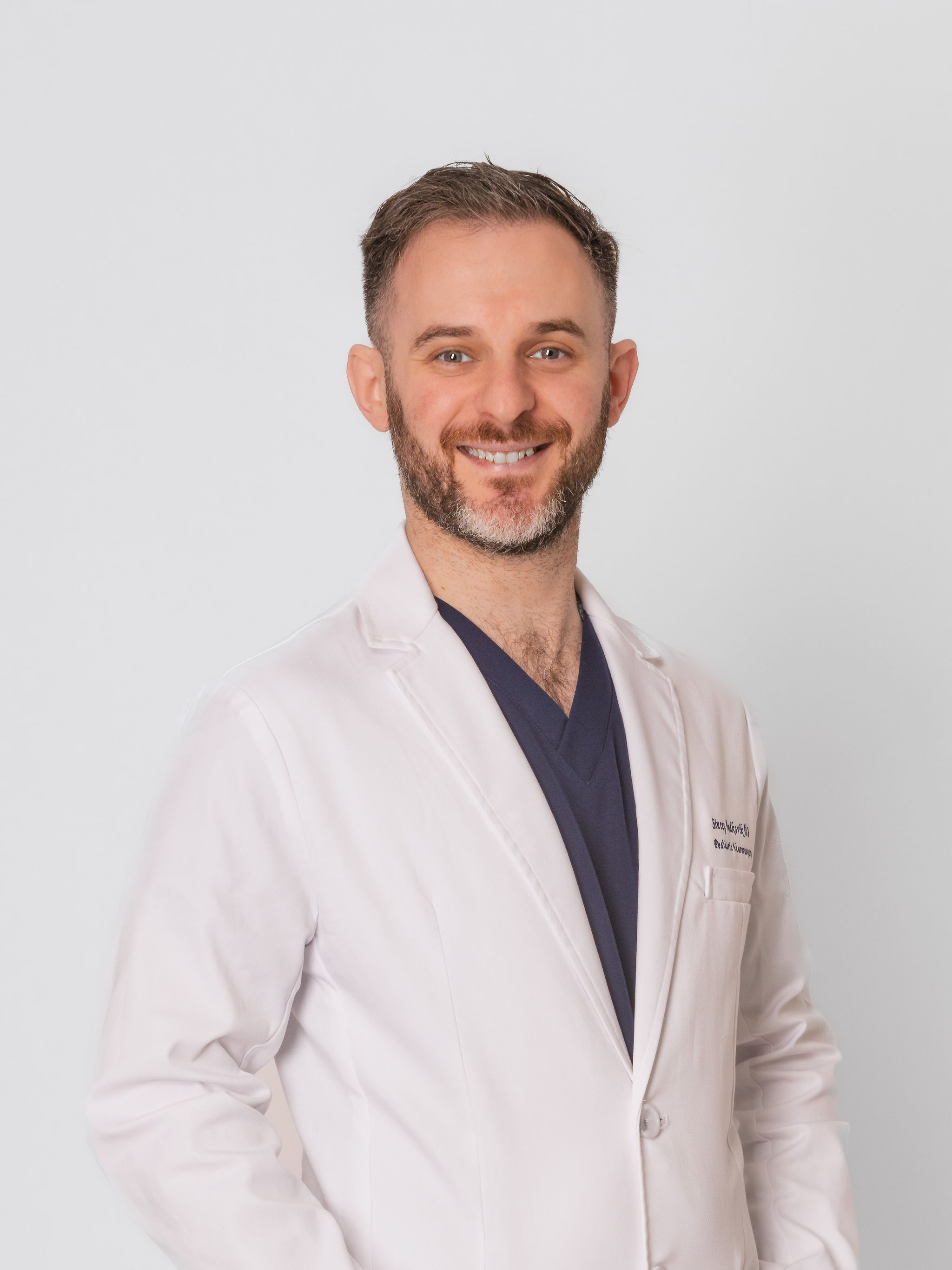 Dr. Stacey Podkovik in his white coat over navy scrubs.