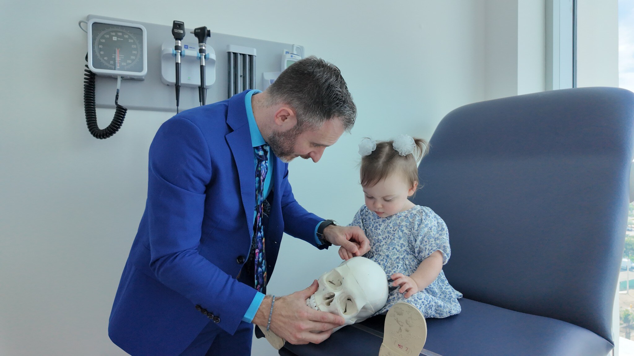 Dr. Stacey in a blue suit helps a child explore a skull model.