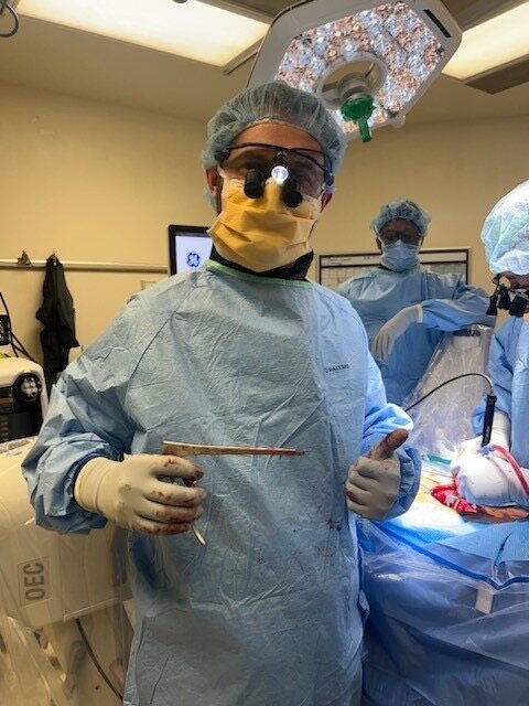 A surgeon wearing a sterile gown, mask and magnifying loupes in the operating room.
